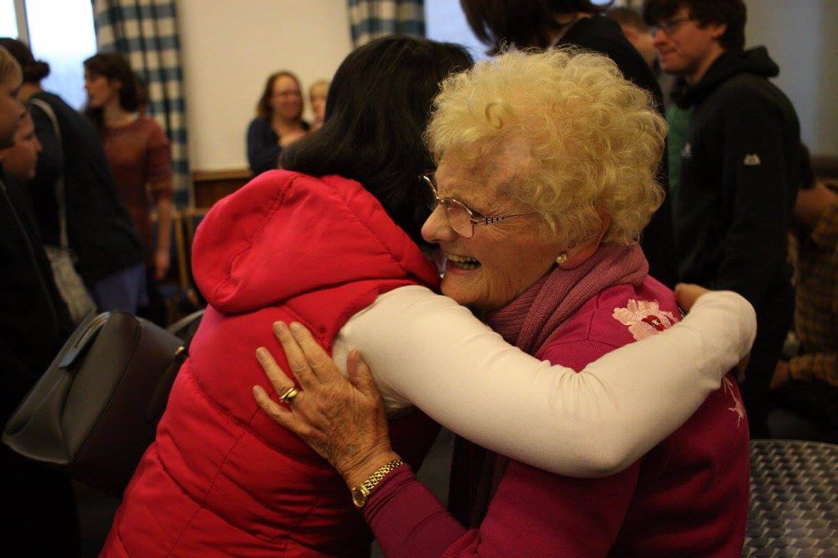 Two women embracing each other in a room full of people